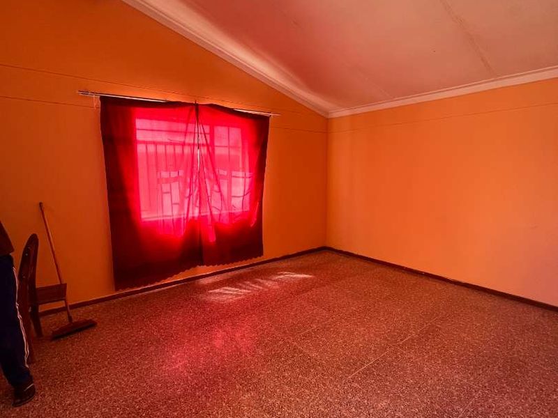 An empty bedroom featuring terrazzo flooring and a vaulted ceiling, awaiting updates to the wall finishes and lighting.