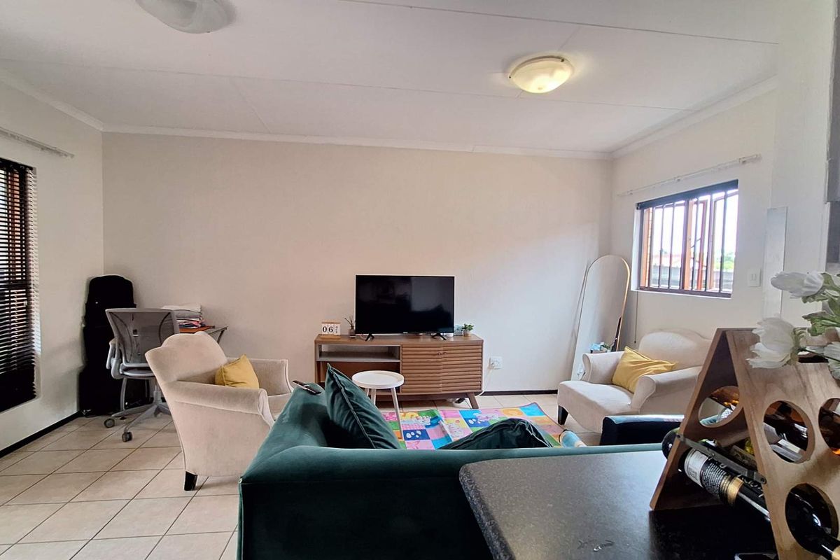 A bright living room featuring tiled flooring, security bars on windows, and neutral wall finishes, offering a functional and comfortable living space.