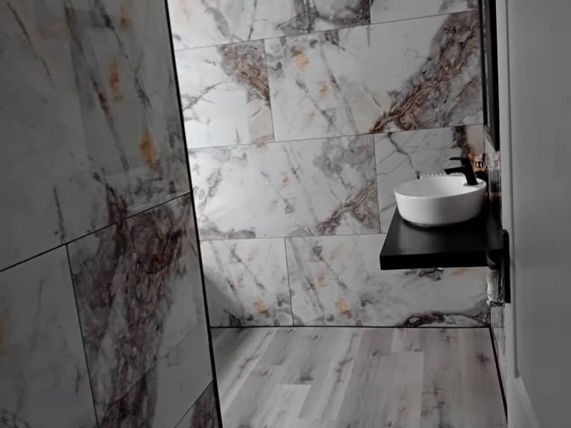 Modern bathroom featuring marble-effect wall tiling, wood-look flooring, and a contemporary vessel sink mounted on a sleek black vanity shelf.