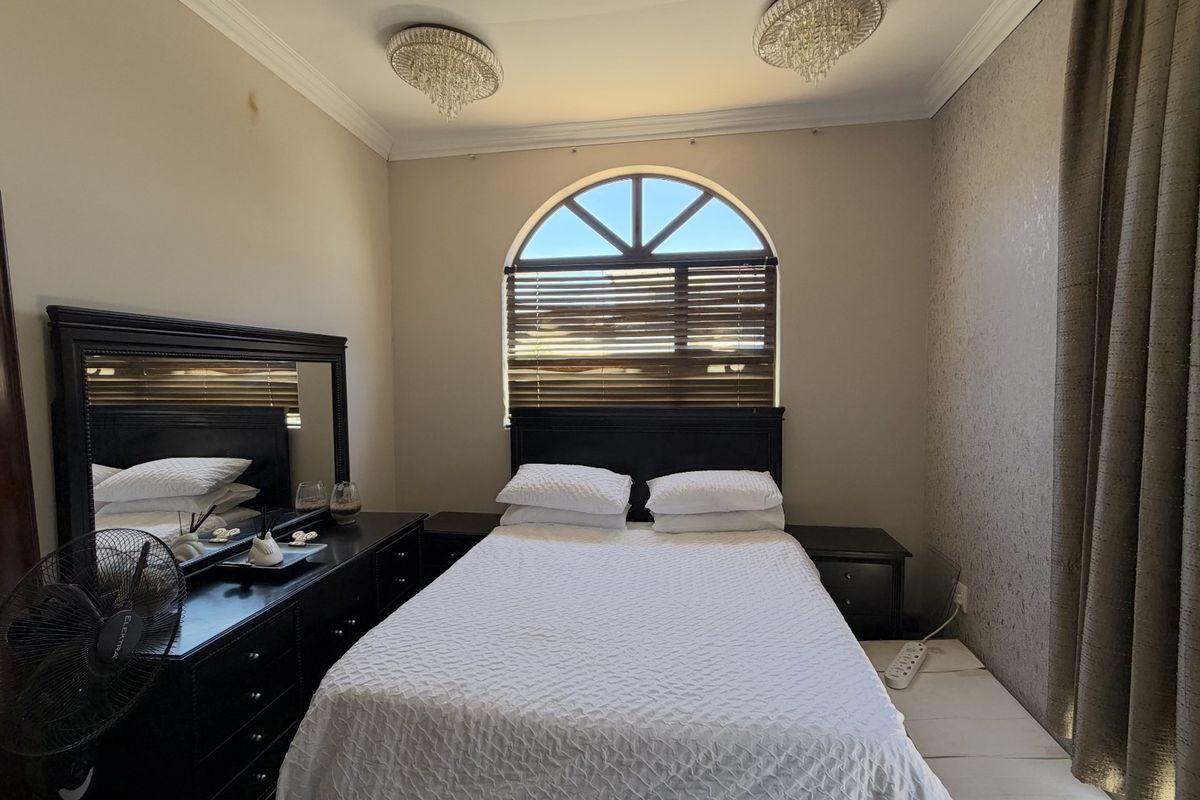 A bedroom featuring an arched window with venetian blinds, crown molding, and decorative crystal light fixtures, with textured wallpaper on the feature wall.
