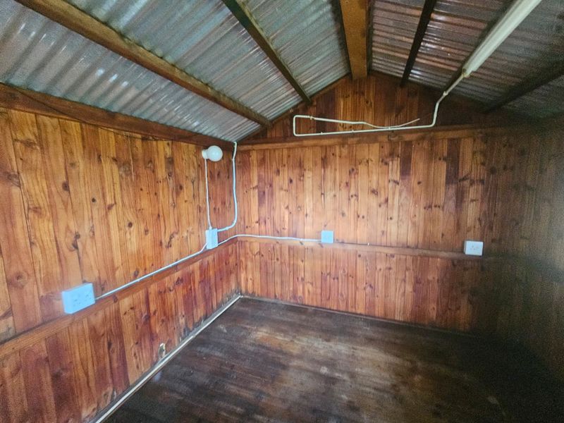 An empty utility space or garden shed featuring timber wall cladding, exposed corrugated metal roofing, and surface-mounted electrical infrastructure.