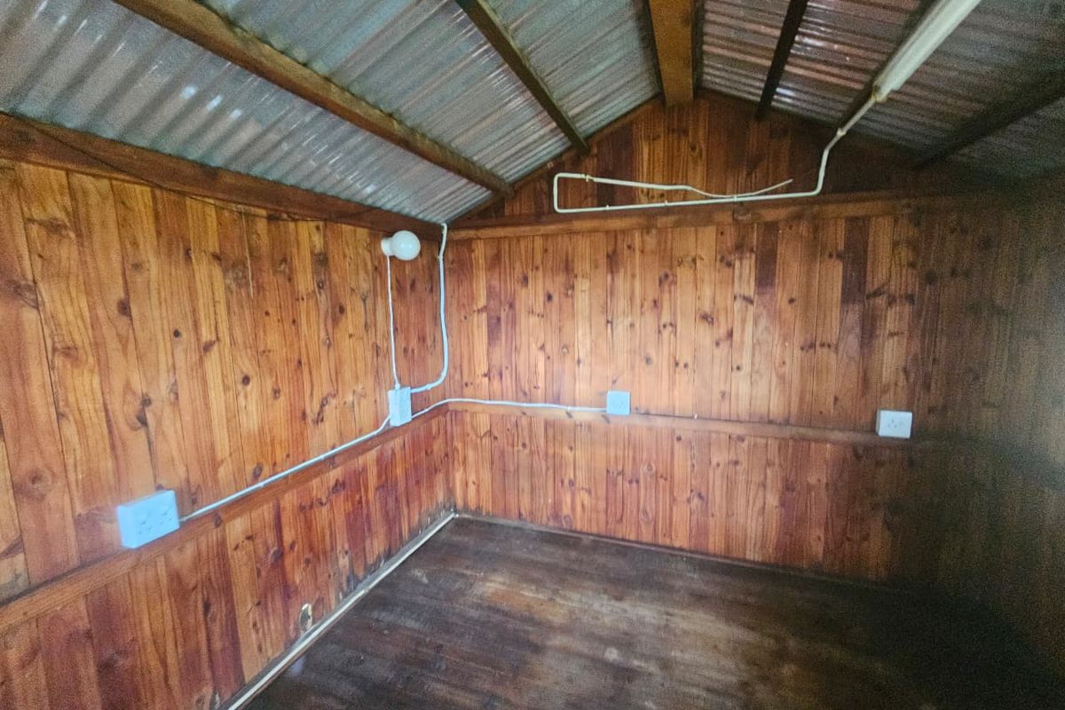 An empty utility space or garden shed featuring timber wall cladding, exposed corrugated metal roofing, and surface-mounted electrical infrastructure.