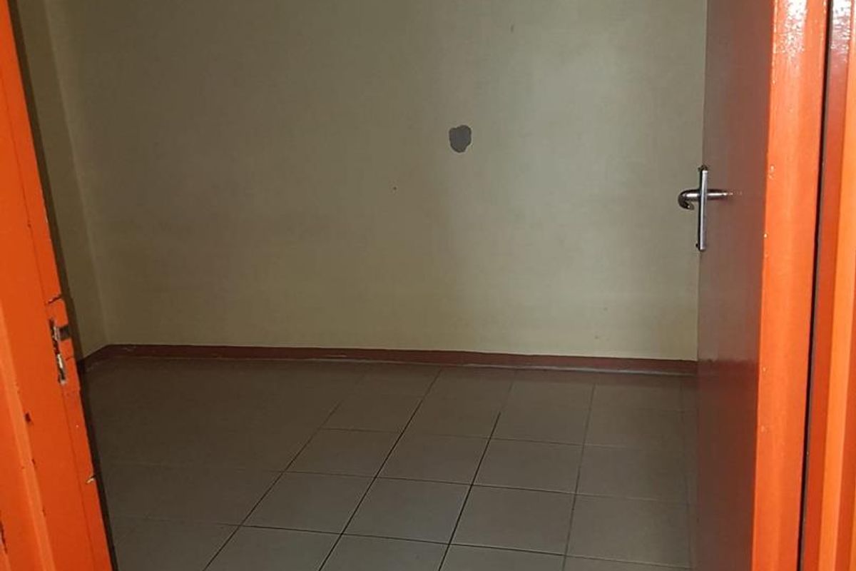 An empty bedroom featuring tiled flooring and plain walls, requiring minor cosmetic repairs to the wall surface and door frame.