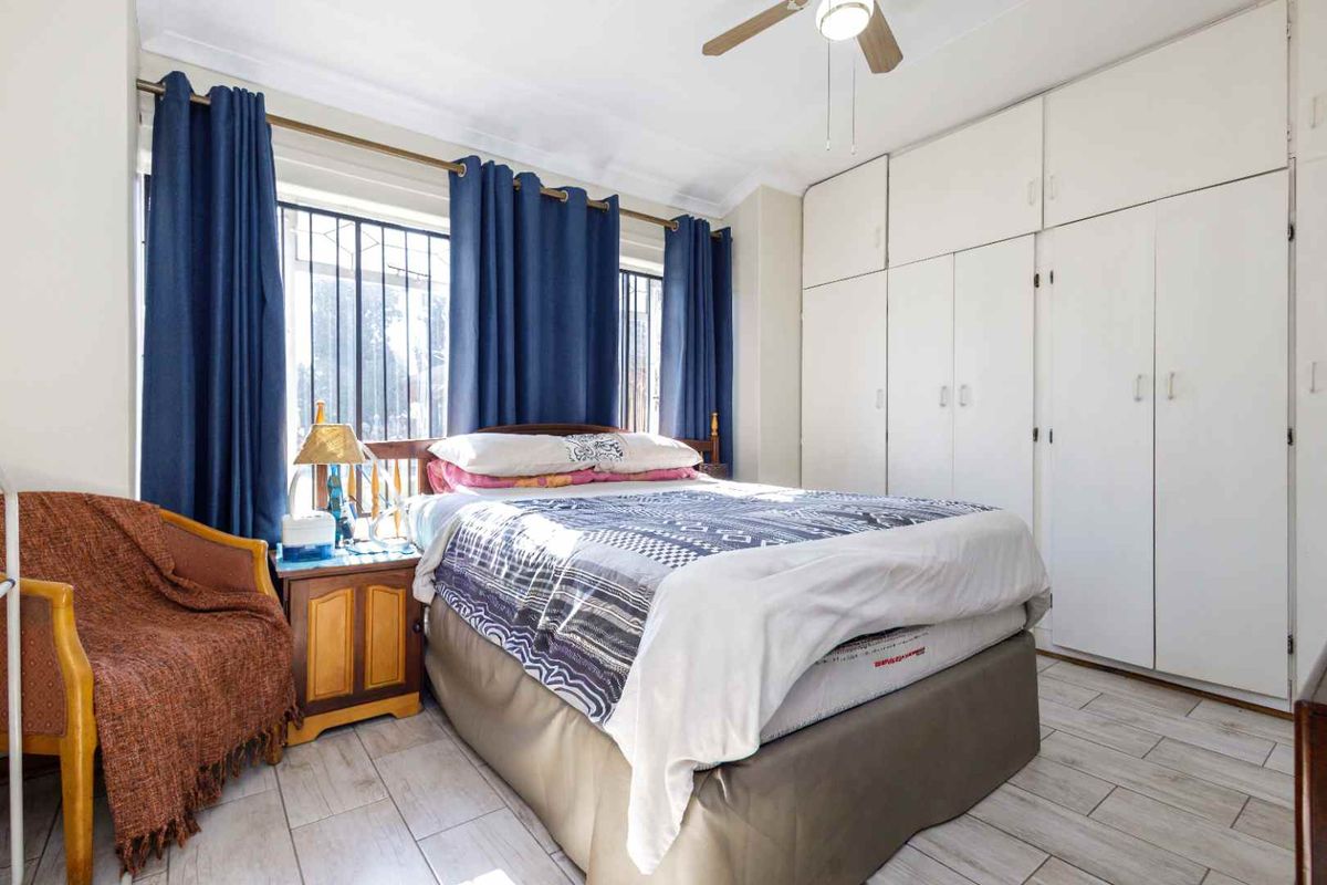 A bedroom featuring built-in cupboards, tiled flooring, and a ceiling fan, with security bars installed on the windows.