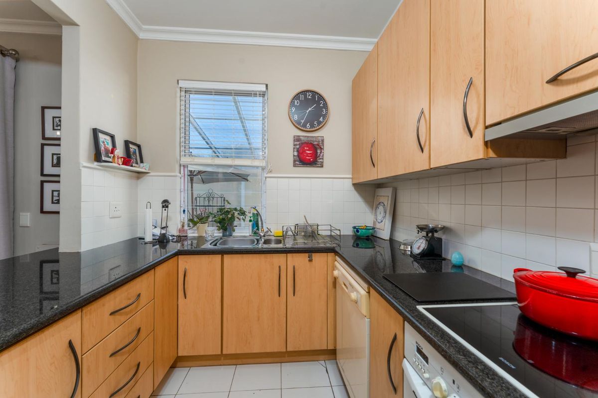 A functional kitchen featuring light wood cabinetry, dark granite countertops, tiled splashbacks, and integrated appliances including a hob and oven.