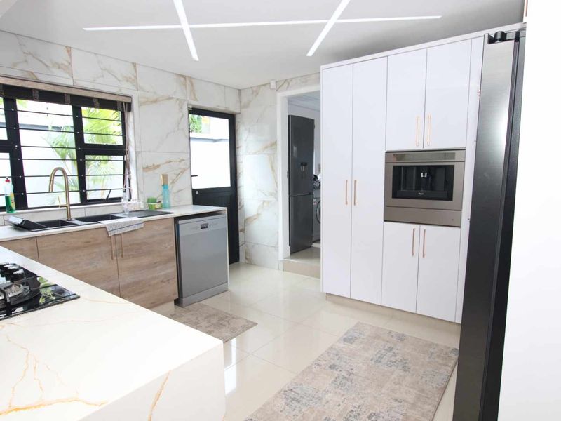 A modern, well-appointed kitchen featuring marble-look wall tiles, sleek white cabinetry, built-in oven, gas hob, and high-quality finishes throughout.