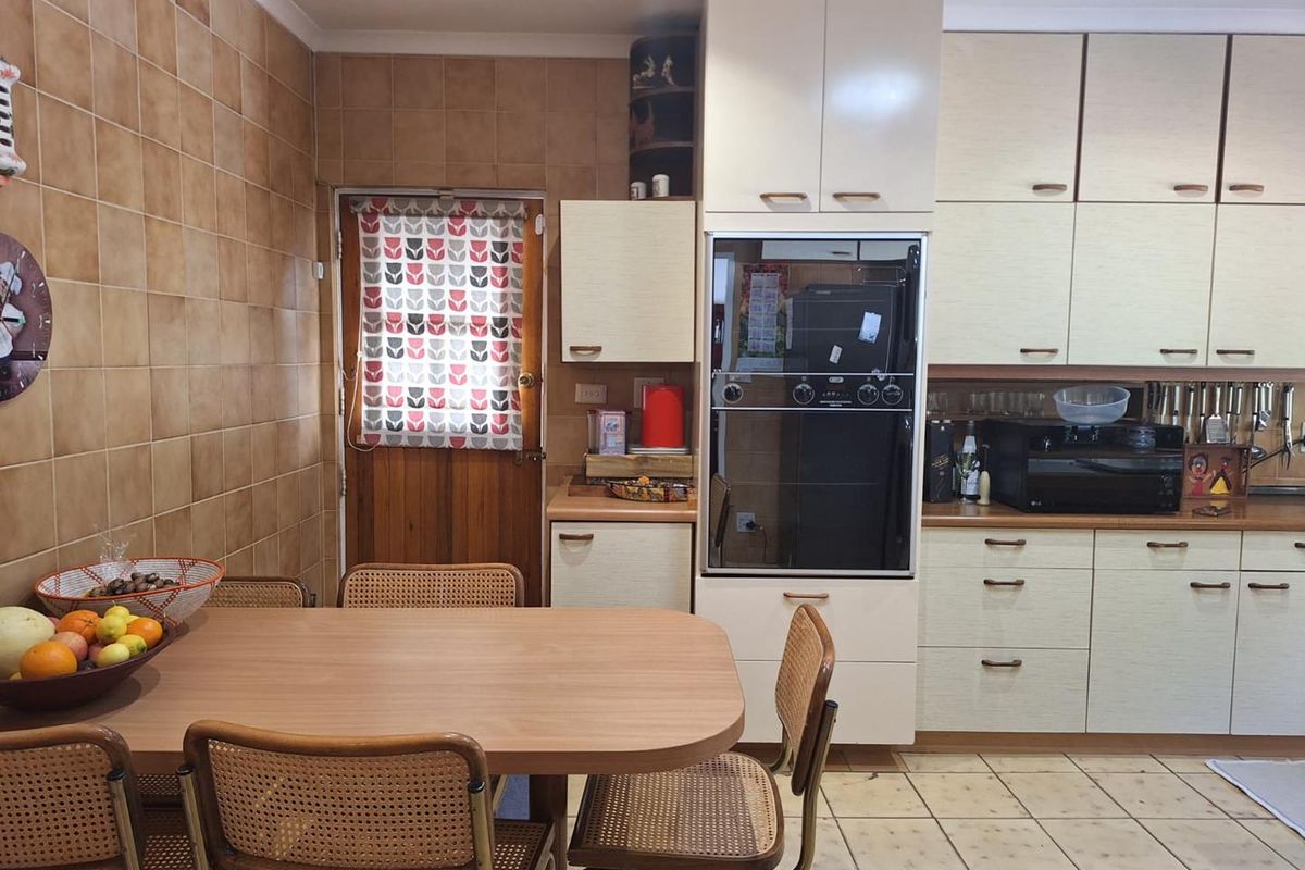 A functional kitchen featuring built-in cabinetry, a wall-mounted oven, and tiled splashbacks, offering a dated aesthetic with potential for modernization.