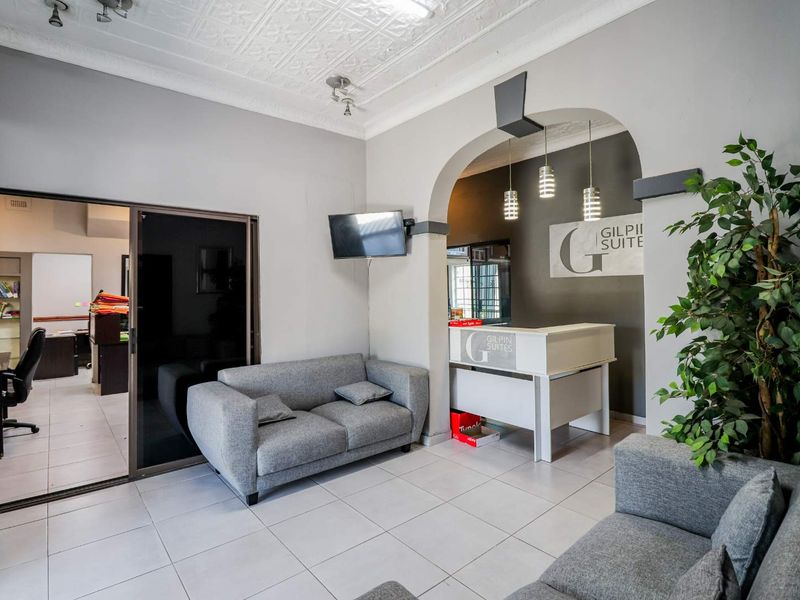 A professional office reception area featuring tiled flooring, a decorative pressed ceiling, and a built-in reception desk with modern pendant lighting.