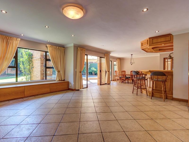 Spacious open-plan living area featuring a built-in bar, tiled flooring, and large sliding doors providing seamless access to the outdoor patio and garden.