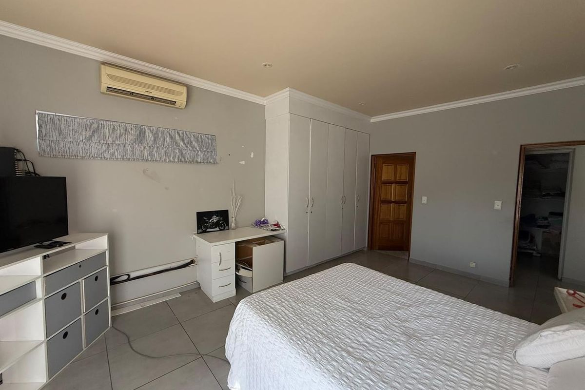 Spacious bedroom featuring built-in cupboards, tiled flooring, and a wall-mounted air conditioning unit.