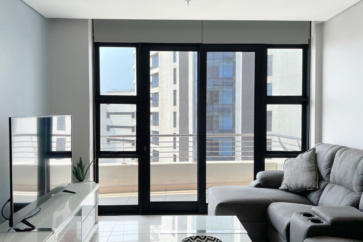 Modern living room featuring large black-framed sliding glass doors that open onto a private balcony with urban views.