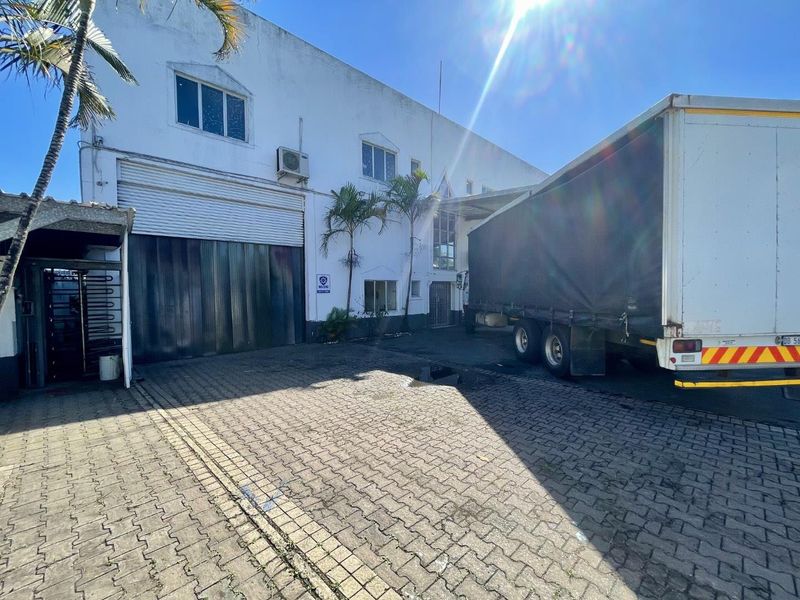 Industrial property exterior featuring a large roller shutter door, paved loading area, and exterior air conditioning unit.