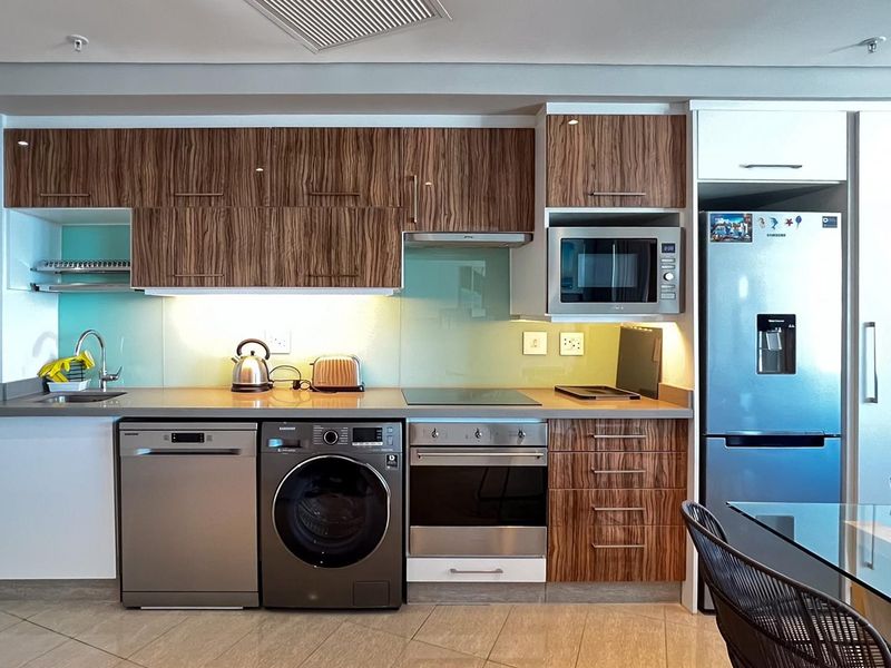 Modern kitchen featuring wood-grain cabinetry, stone countertops, glass splashback, and integrated stainless steel appliances including an oven, cooktop, and microwave.