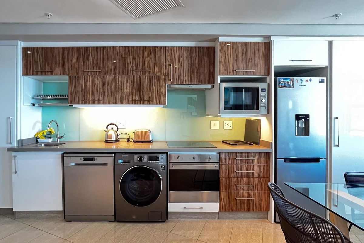 Modern kitchen featuring wood-grain cabinetry, stone countertops, glass splashback, and integrated stainless steel appliances including an oven, cooktop, and microwave.
