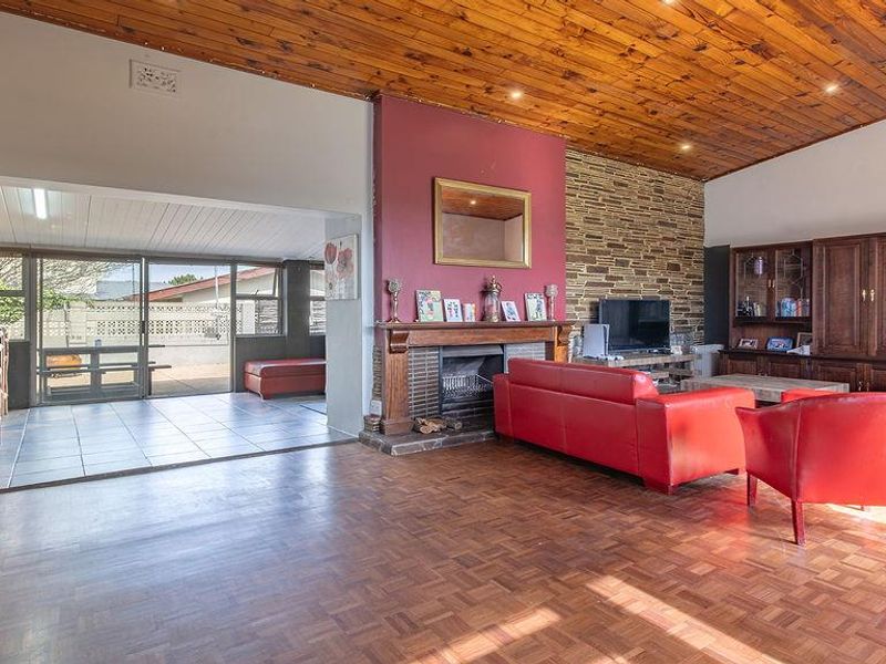 Spacious open-plan living area featuring a stone fireplace, timber-clad vaulted ceiling, parquet flooring, and an integrated bar area leading to an outdoor space.