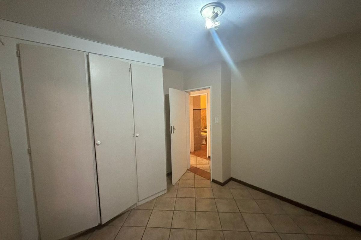 An empty bedroom featuring tiled flooring and built-in cupboards, with a doorway leading to an adjacent bathroom.