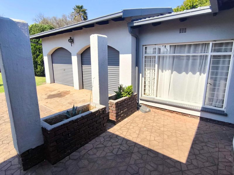 Rear exterior view featuring a paved patio area, brick planter boxes, and access to a double garage with roller doors.