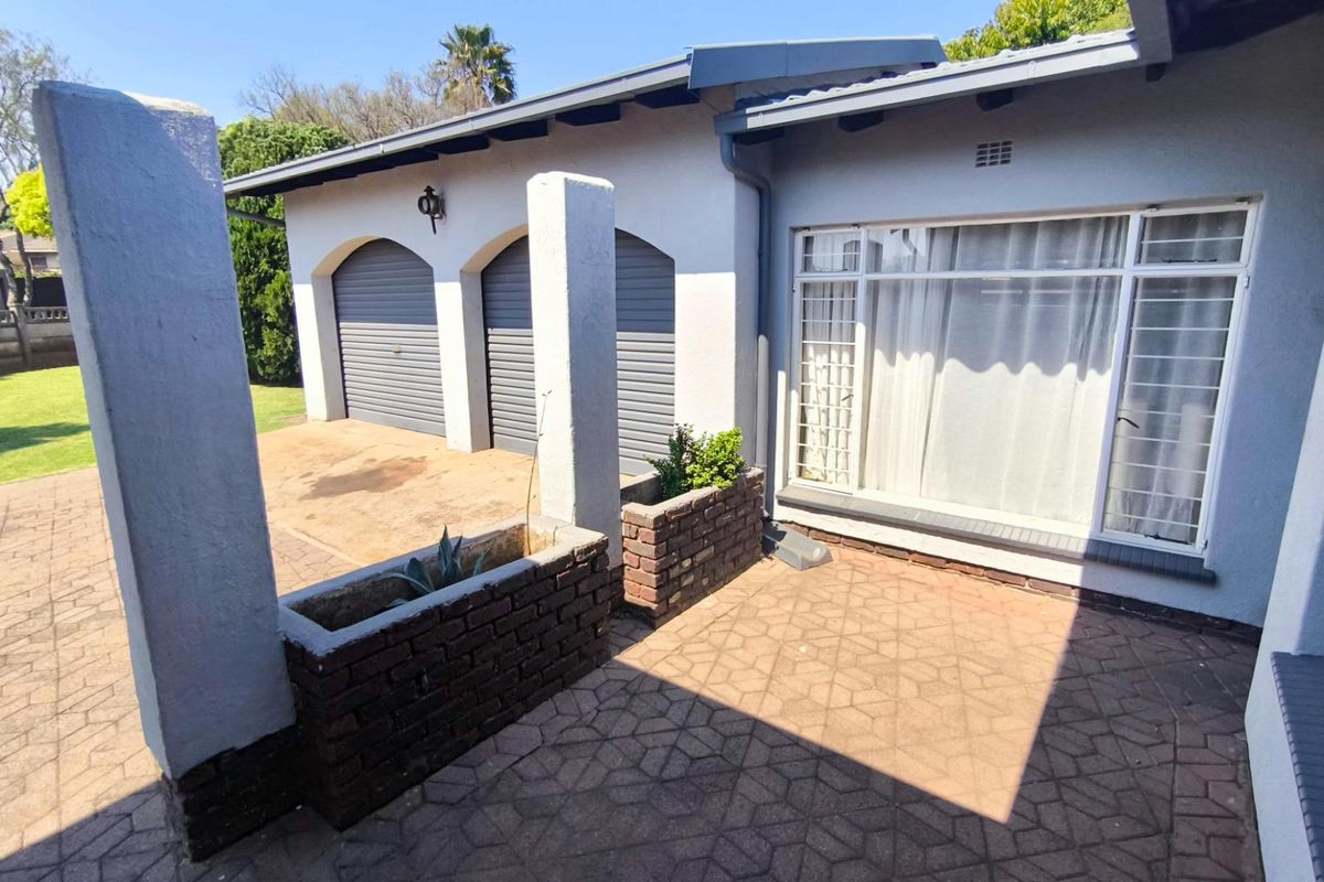 Rear exterior view featuring a paved patio area, brick planter boxes, and access to a double garage with roller doors.