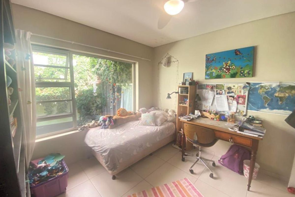 A bright bedroom featuring large windows with garden views, tiled flooring, and a ceiling fan.