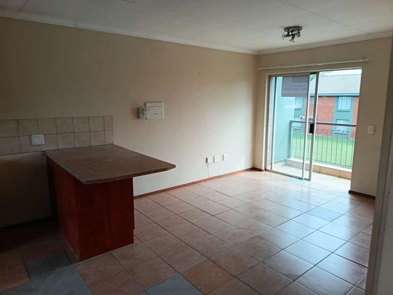 An empty open-plan living area featuring tiled flooring, a breakfast counter, and a sliding door leading to a balcony.