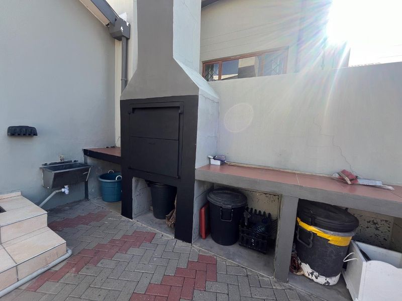 Outdoor patio area featuring a built-in braai, tiled prep surfaces, and a small utility sink, providing a functional space for outdoor cooking and entertaining.