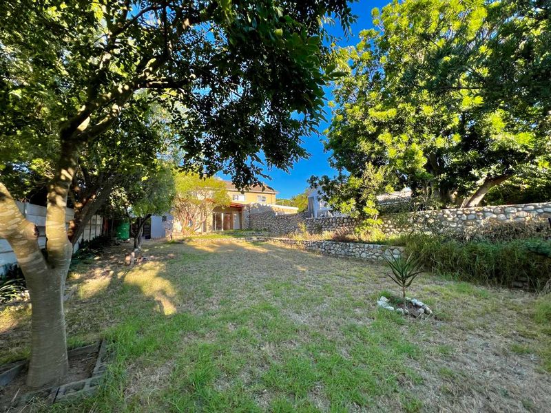 A spacious rear garden featuring a stone retaining wall, mature trees, and a lawn area, providing a private outdoor space.