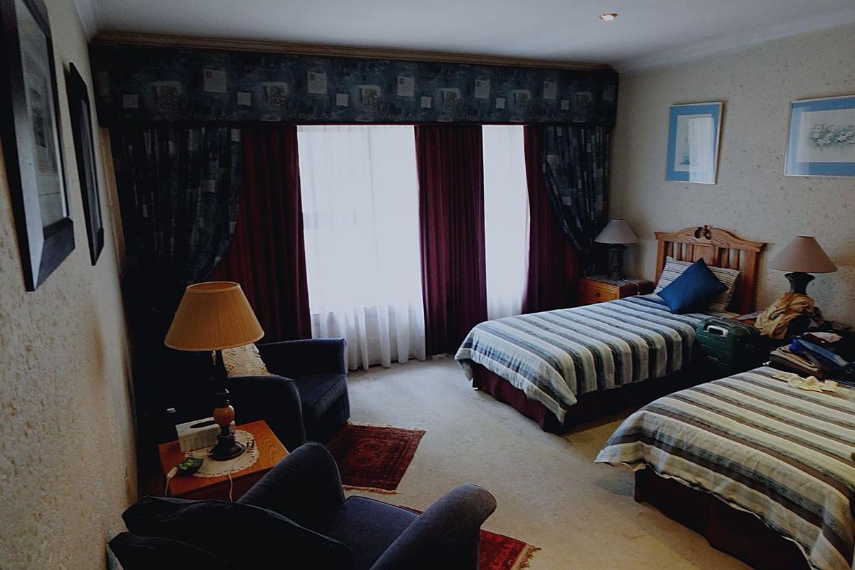 A bedroom featuring twin beds, carpeted flooring, and a large window with heavy drapery.