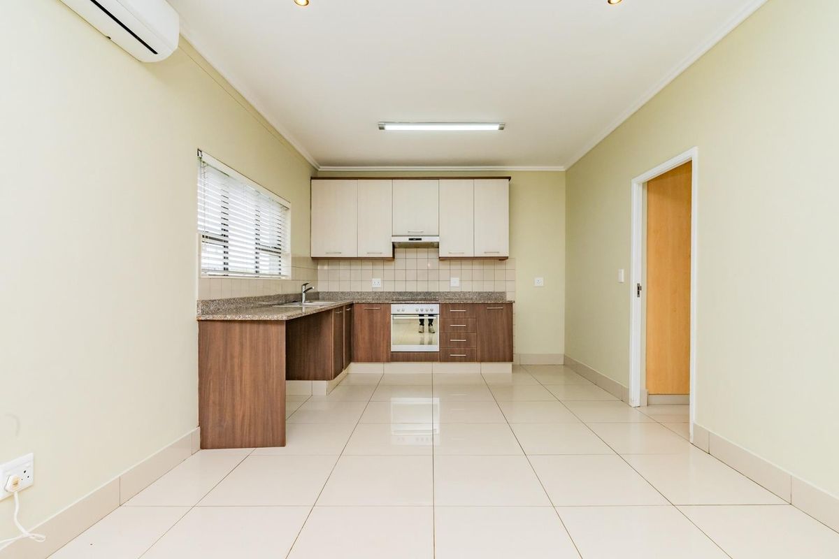 A clean, modern kitchen featuring two-tone cabinetry, granite countertops, built-in oven with extractor, and neutral tiled flooring in an open-plan layout.
