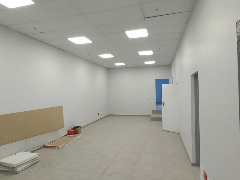 A clean, vacant industrial office space featuring neutral walls, tiled flooring, and modern recessed LED panel lighting in a suspended ceiling.