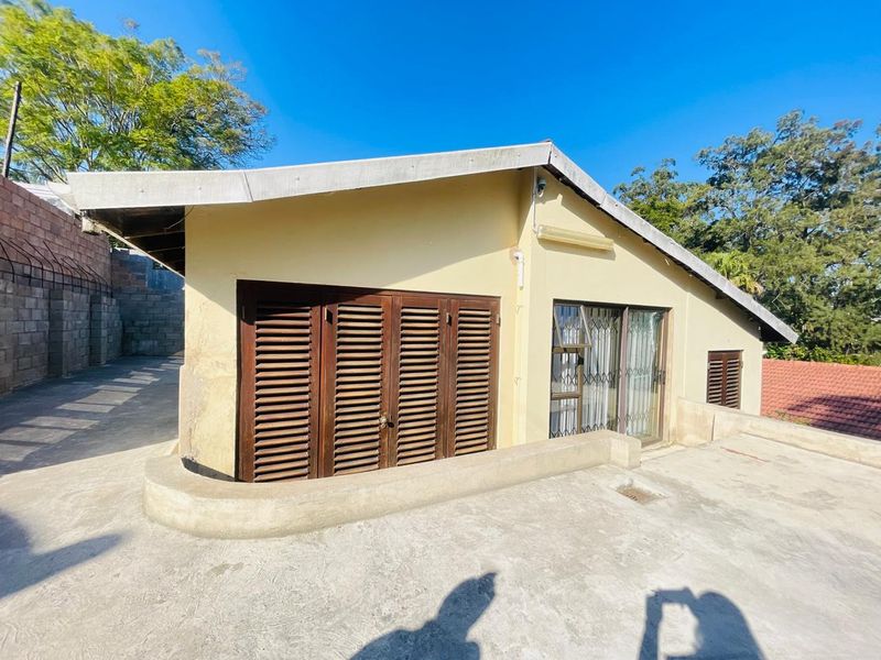 Rear exterior view of the property featuring a concrete patio area, wooden shutters, and a sliding glass door with security gate.