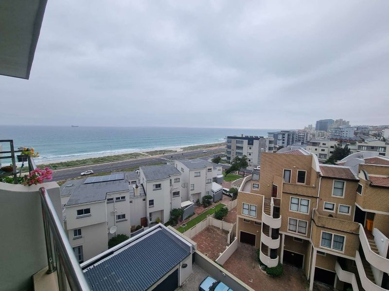 Elevated coastal view overlooking the ocean, beach road, and surrounding residential apartment complex.