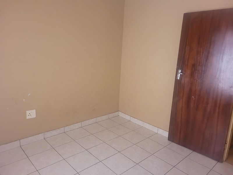 An empty bedroom featuring neutral wall paint, tiled flooring, and a wooden door.