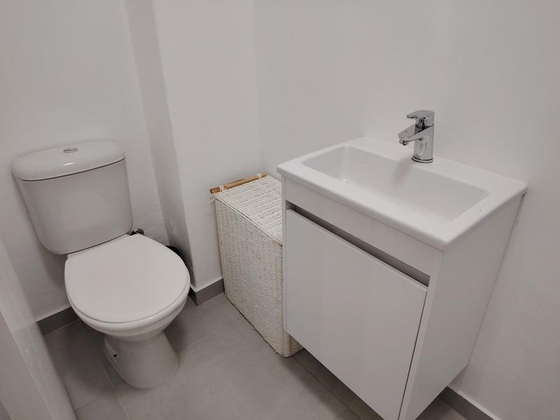 A clean and modern bathroom featuring a white vanity cabinet with a basin, chrome faucet, and a standard toilet.