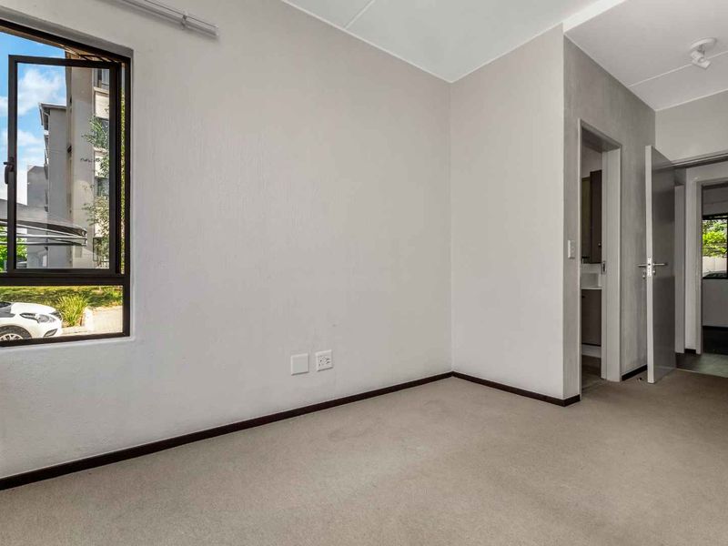 An empty bedroom featuring neutral walls, carpeted flooring, and an aluminium window frame, offering a blank canvas for personalization.