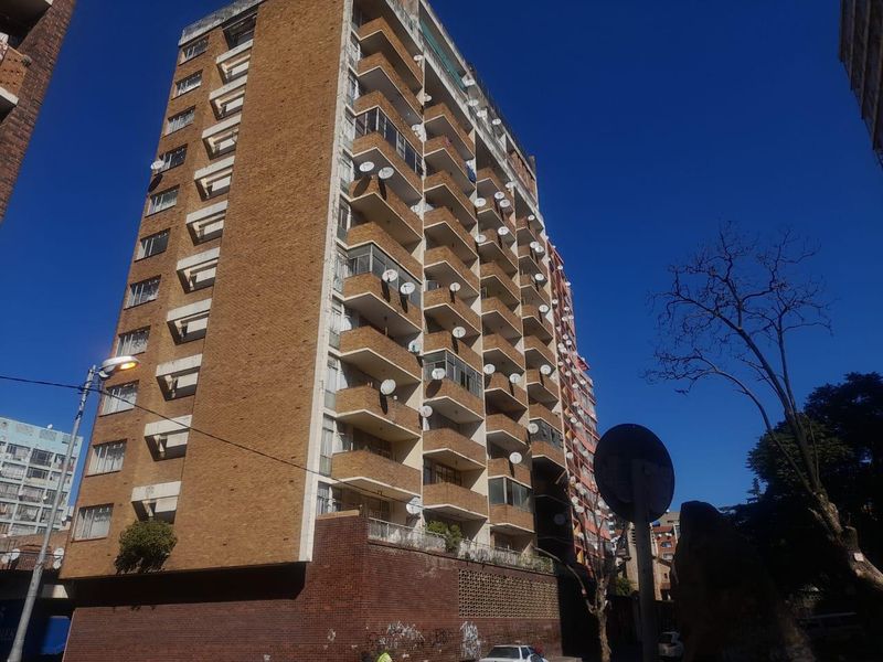 Exterior view of a multi-story brick apartment building featuring multiple balconies and numerous satellite dishes mounted on the facade.