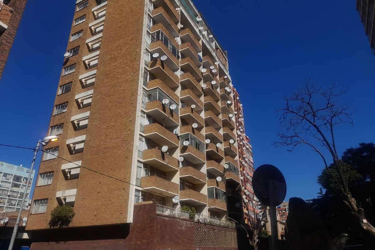 Exterior view of a multi-story brick apartment building featuring multiple balconies and numerous satellite dishes mounted on the facade.