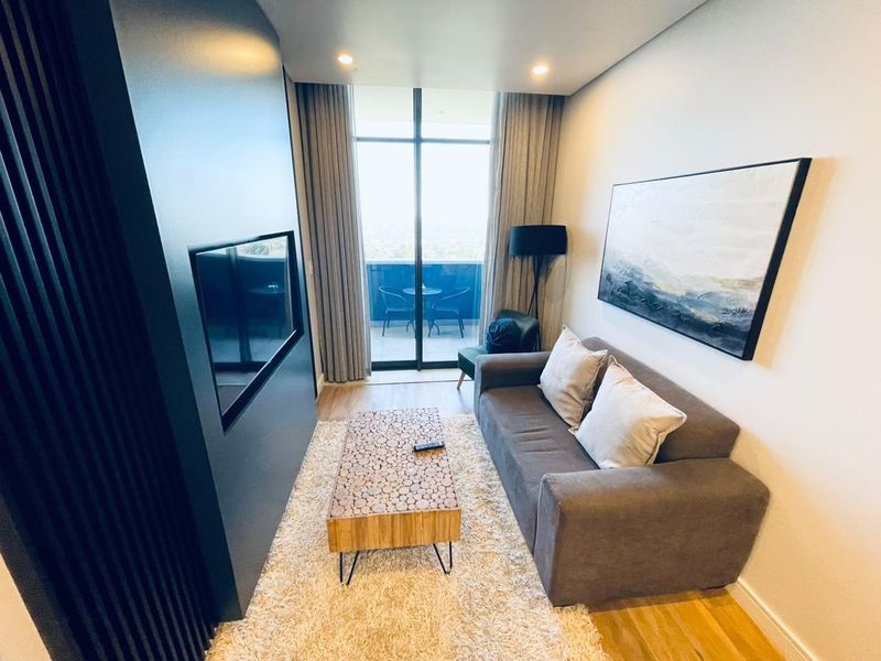 A modern, well-maintained living room featuring timber flooring, a sleek built-in media wall, and large sliding glass doors leading to a private balcony.