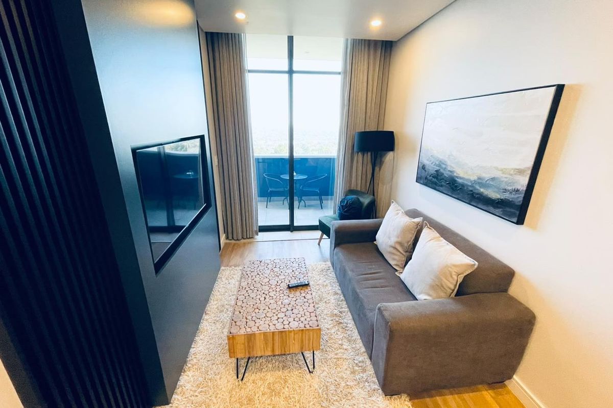 A modern, well-maintained living room featuring timber flooring, a sleek built-in media wall, and large sliding glass doors leading to a private balcony.