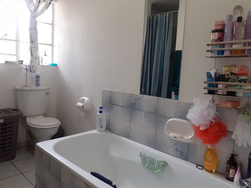 A functional bathroom featuring a standard bathtub, toilet, and tiled splashback, requiring cosmetic updates to improve its overall condition and aesthetic appeal.