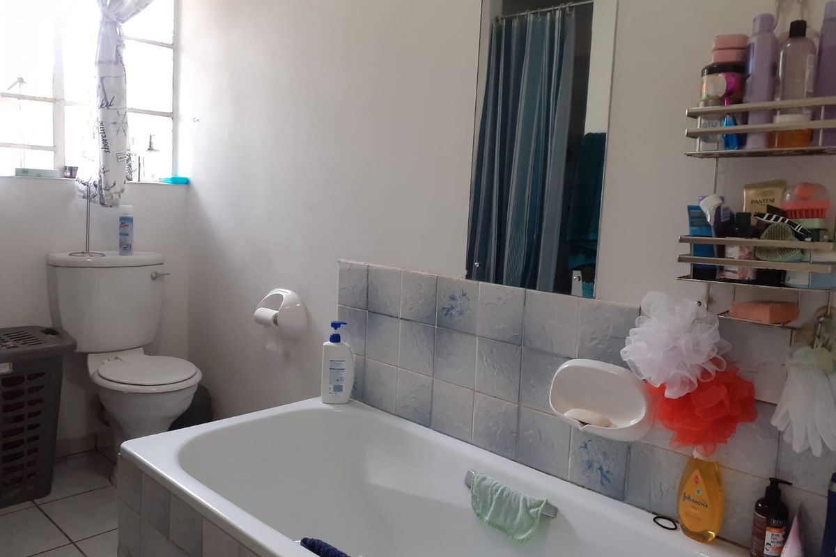 A functional bathroom featuring a standard bathtub, toilet, and tiled splashback, requiring cosmetic updates to improve its overall condition and aesthetic appeal.