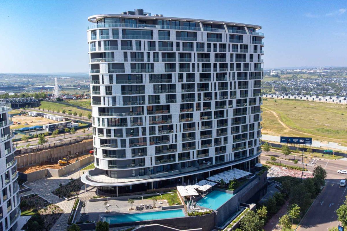 Aerial view of a modern high-rise penthouse building featuring glass balconies, a swimming pool area, and landscaped surroundings in a contemporary urban development.