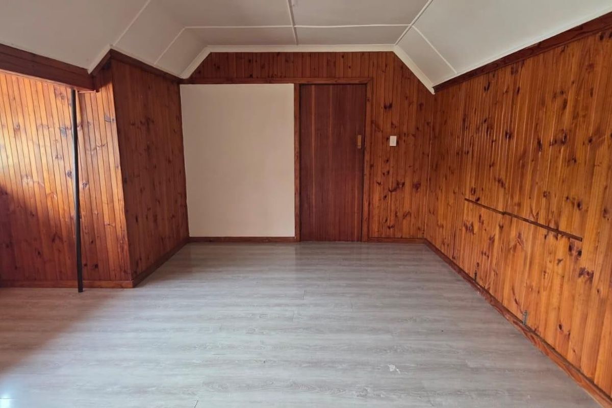 An empty bedroom featuring dated timber wall paneling, light-toned laminate flooring, and security bars on the window.