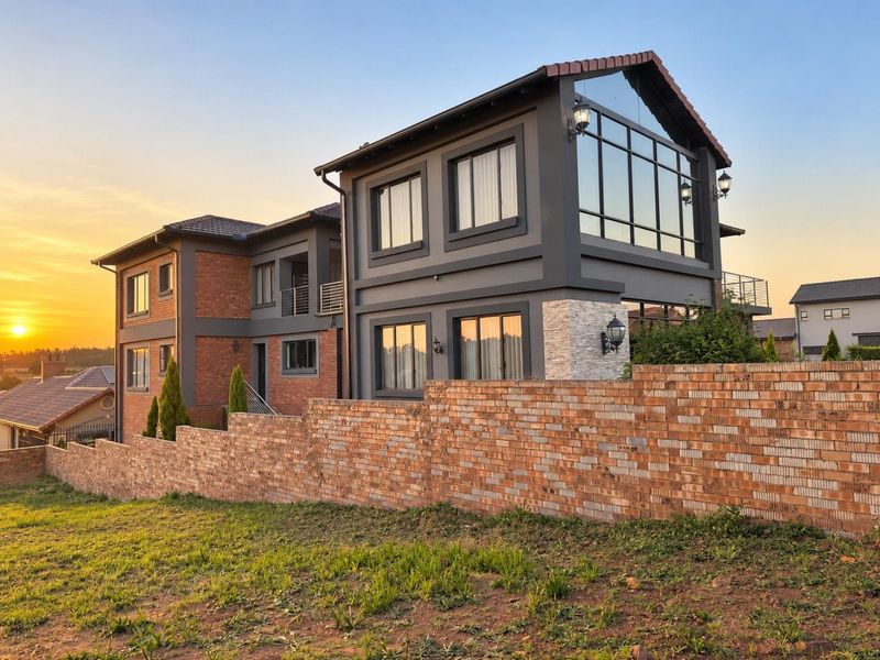 A modern double-story residence featuring a striking combination of brick and dark grey finishes, large glass windows, and a prominent brick boundary wall.