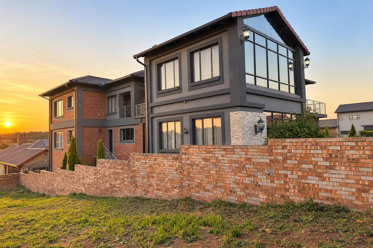 A modern double-story residence featuring a striking combination of brick and dark grey finishes, large glass windows, and a prominent brick boundary wall.
