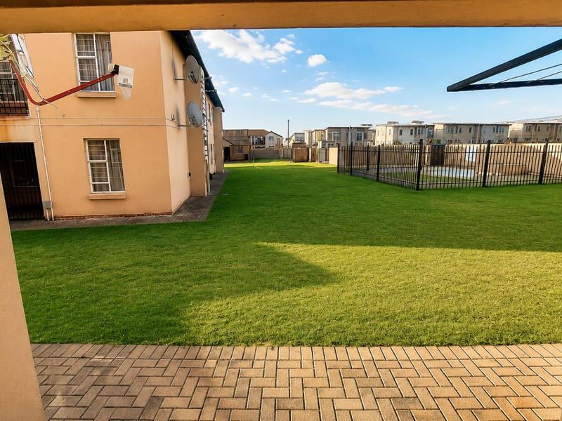 A view of the rear communal garden area featuring a paved patio, well-maintained lawn, and a fenced swimming pool.