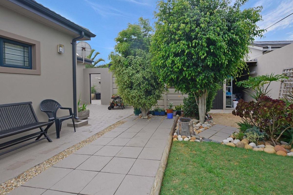 A well-maintained rear garden area featuring paved walkways, established trees, and a small lawn, providing a pleasant outdoor space.