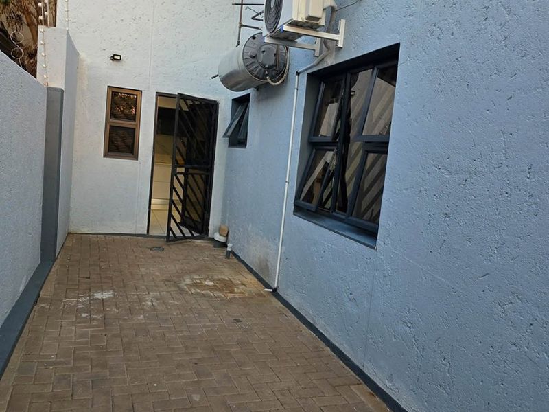 A paved rear courtyard area featuring an external geyser, air conditioning unit, and security gate access to the interior.
