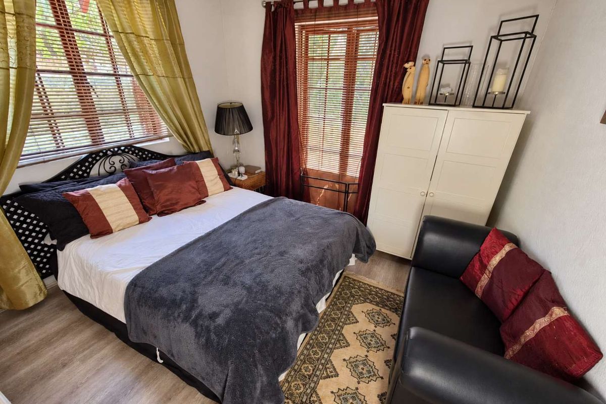 A cozy bedroom featuring light-toned laminate flooring and dual windows fitted with wooden venetian blinds, offering a functional and comfortable sleeping space.