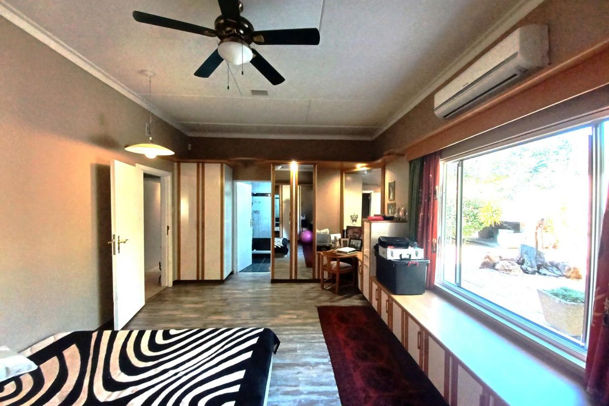 Spacious bedroom featuring built-in cabinetry, a ceiling fan, wall-mounted air conditioning unit, and large windows overlooking the garden area.