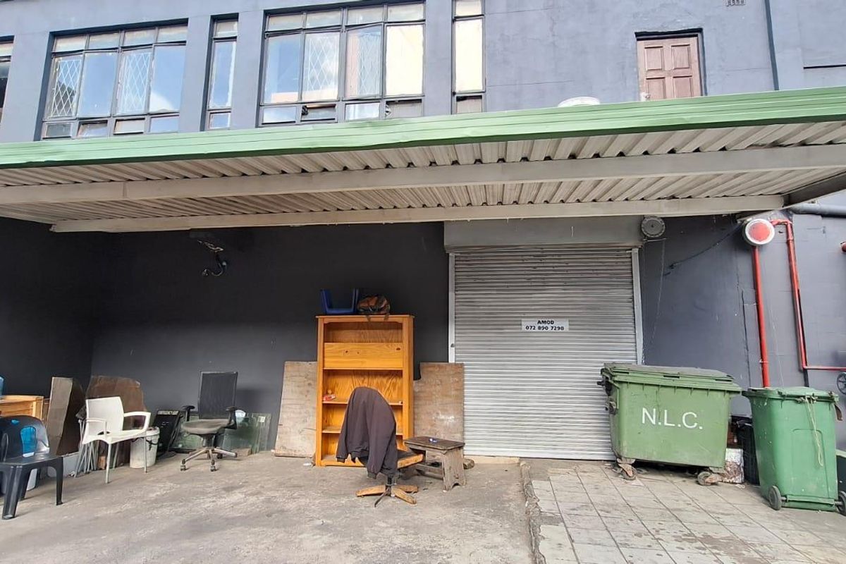 Rear industrial exterior area featuring a metal roller shutter door, corrugated awning, and exposed fire suppression piping against a dark painted facade.